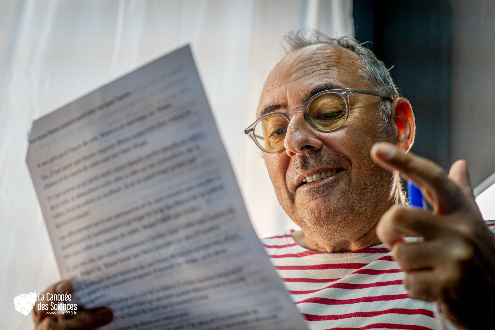 Un homme portant des lunettes tient un morceau de papier et le pointe du doigt.