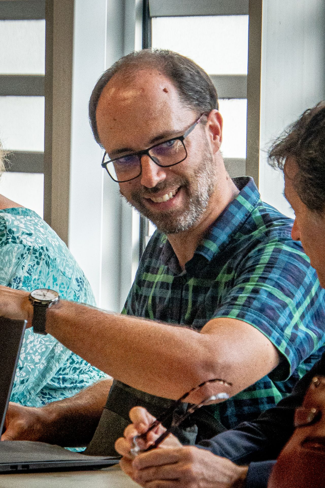 Un homme portant des lunettes sourit assis à une table avec d'autres personnes.