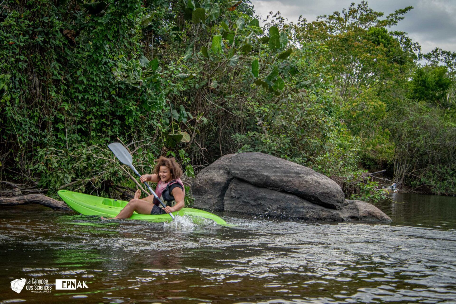 Une femme pagaie dans un kayak vert dans une rivière.