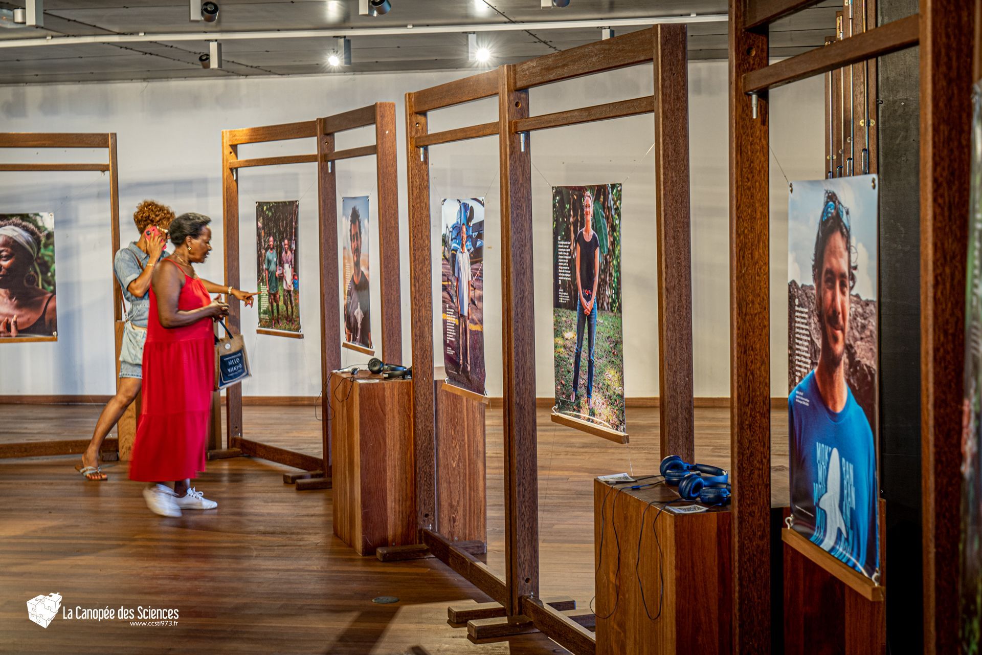 Une femme en robe rouge se tient dans une pièce avec beaucoup de photos sur le mur.