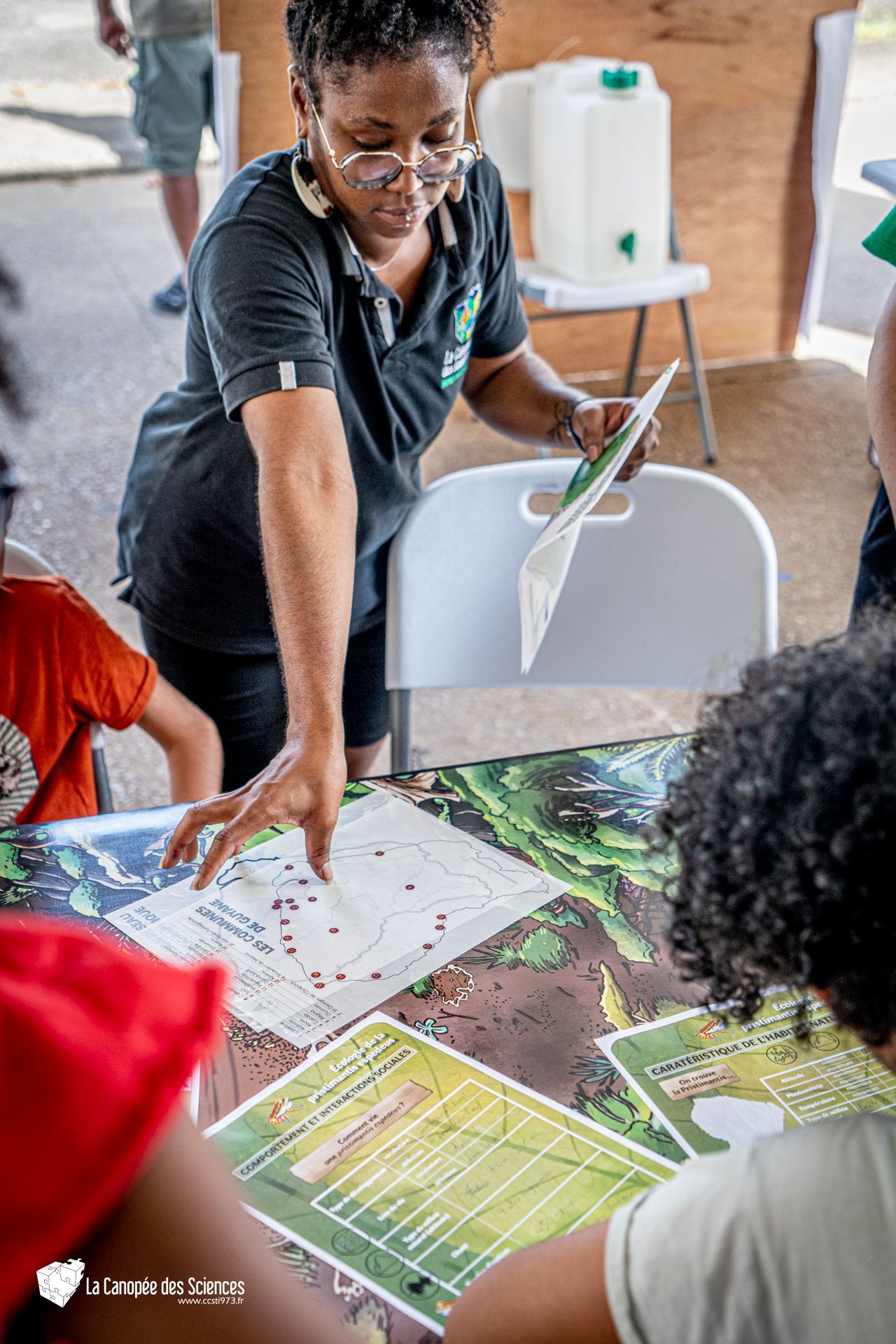 Une femme est debout à une table et parle à un groupe d'enfants.