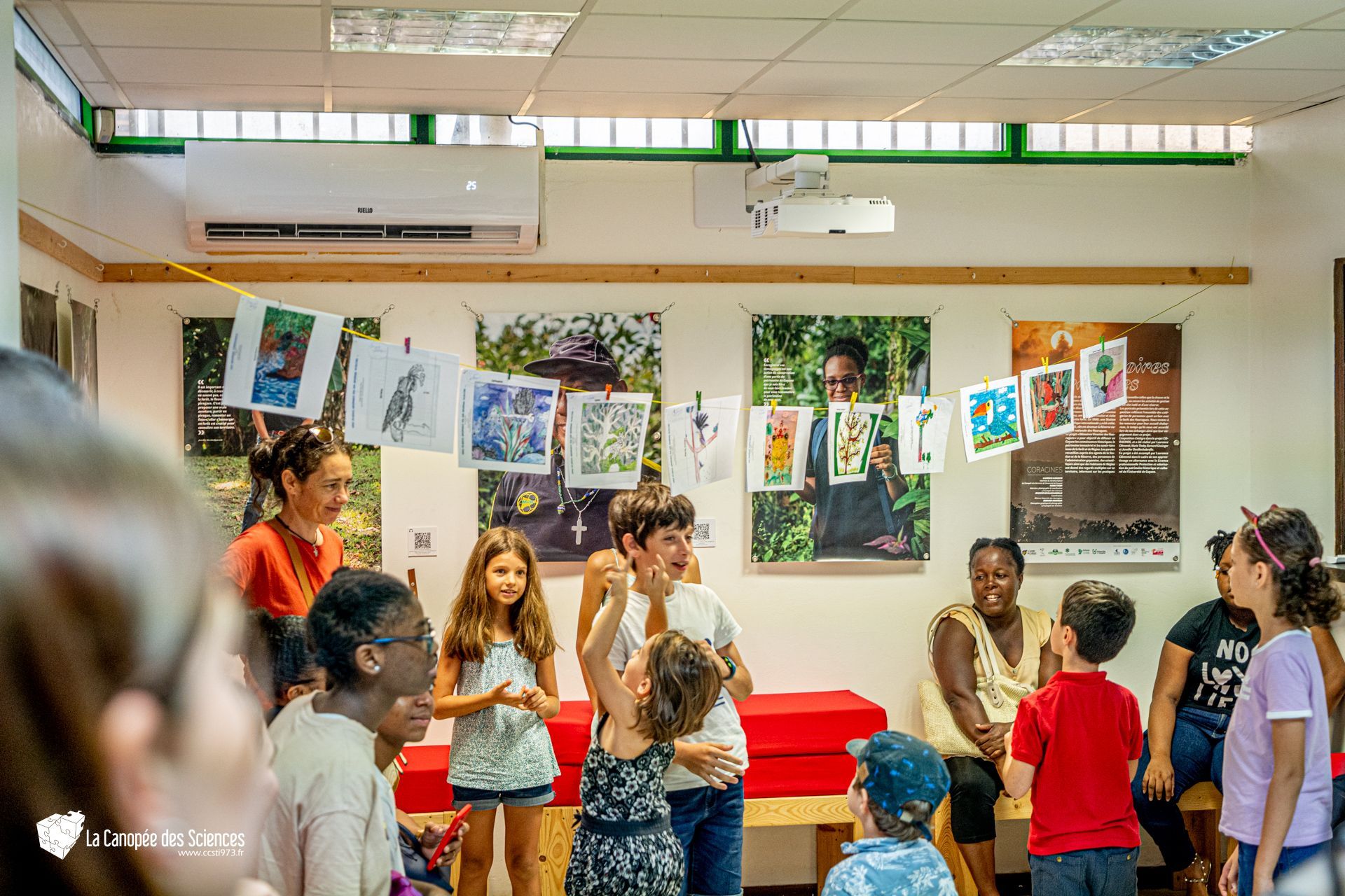 Un groupe d'enfants se tient dans une pièce avec des images accrochées au plafond.