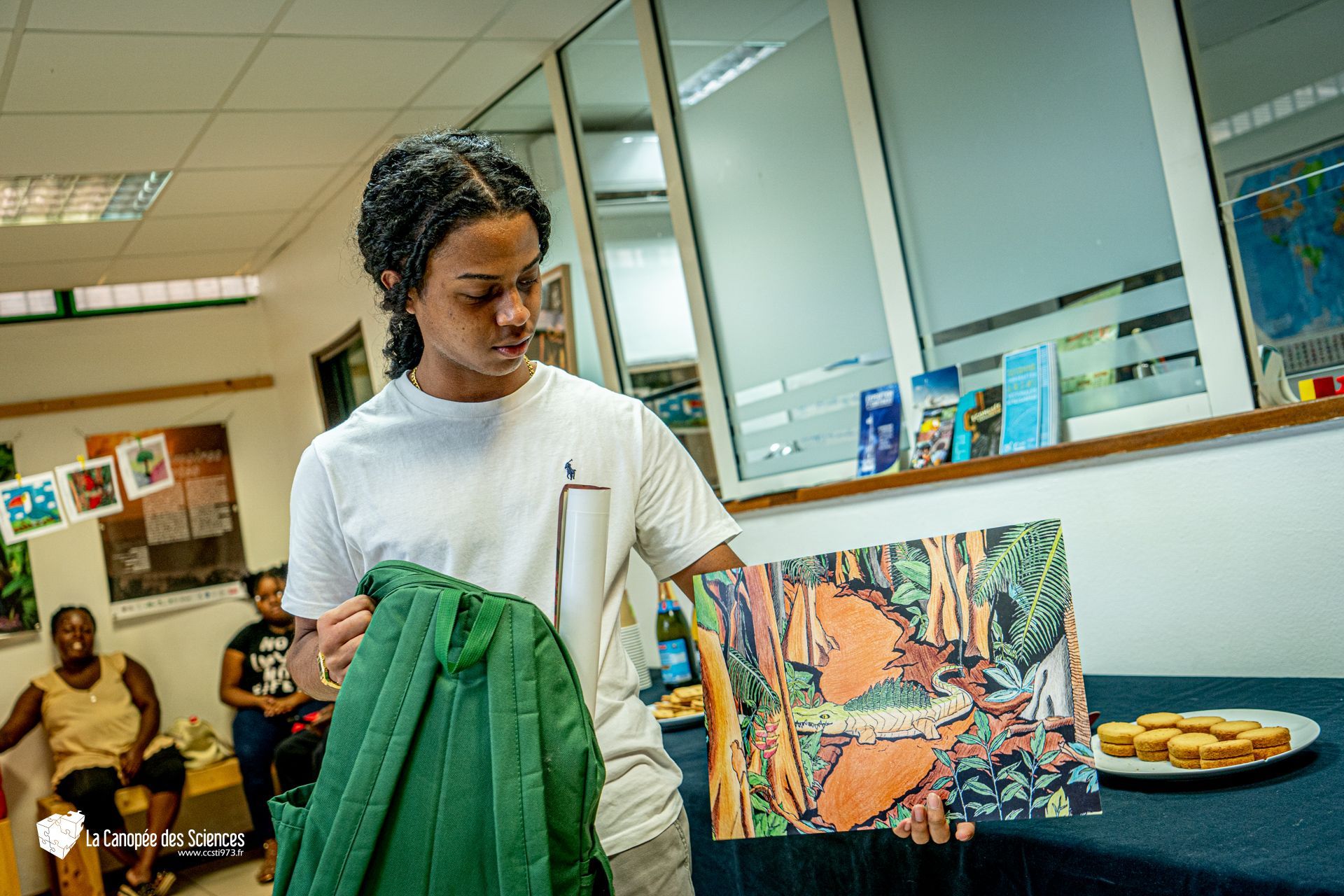 Un homme tient une veste verte et un tableau dans une pièce.