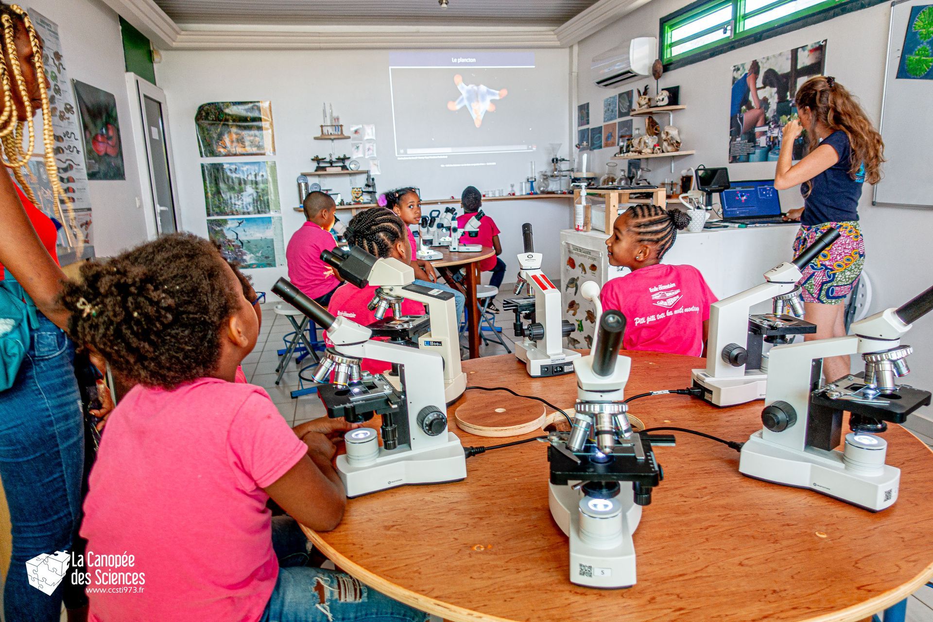 Un groupe d'enfants regardent à travers des microscopes dans une salle de classe.