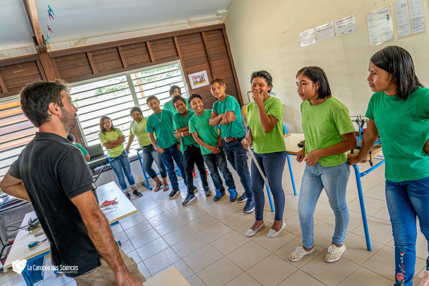 Un groupe de personnes en chemises vertes se tient autour d'un homme dans une salle de classe.
