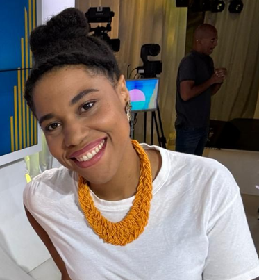 Une femme avec des tresses sourit et fait un signe de paix.