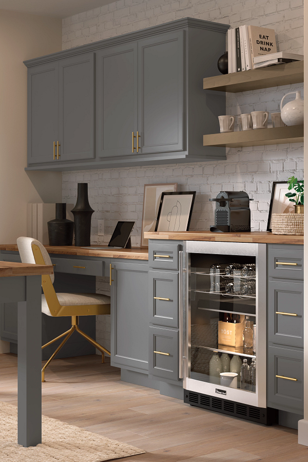 A kitchen with gray cabinets , a refrigerator , a desk and a chair.