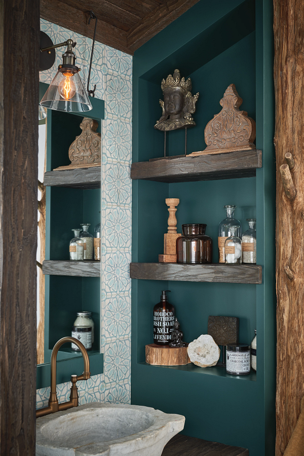 A bathroom with a sink , mirror and shelves filled with bottles.