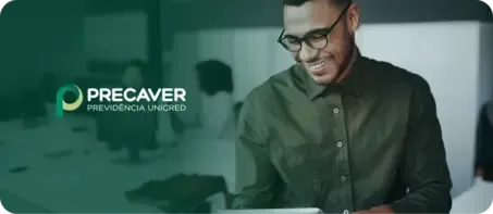 Um homem sorridente, de óculos e camisa verde, em um escritório. O logotipo da Precaver está no canto superior esquerdo.