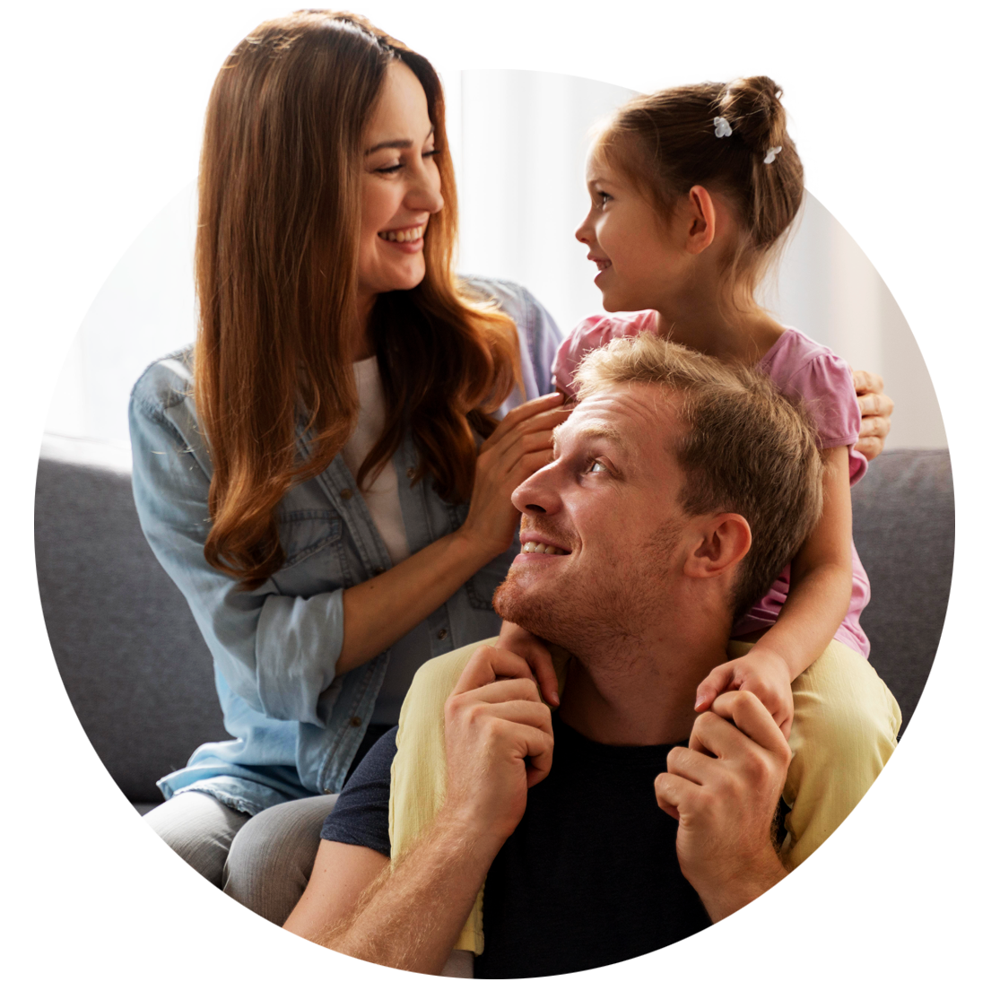 Família de três pessoas sorrindo, filha nos ombros do pai, mãe ao lado deles no sofá.