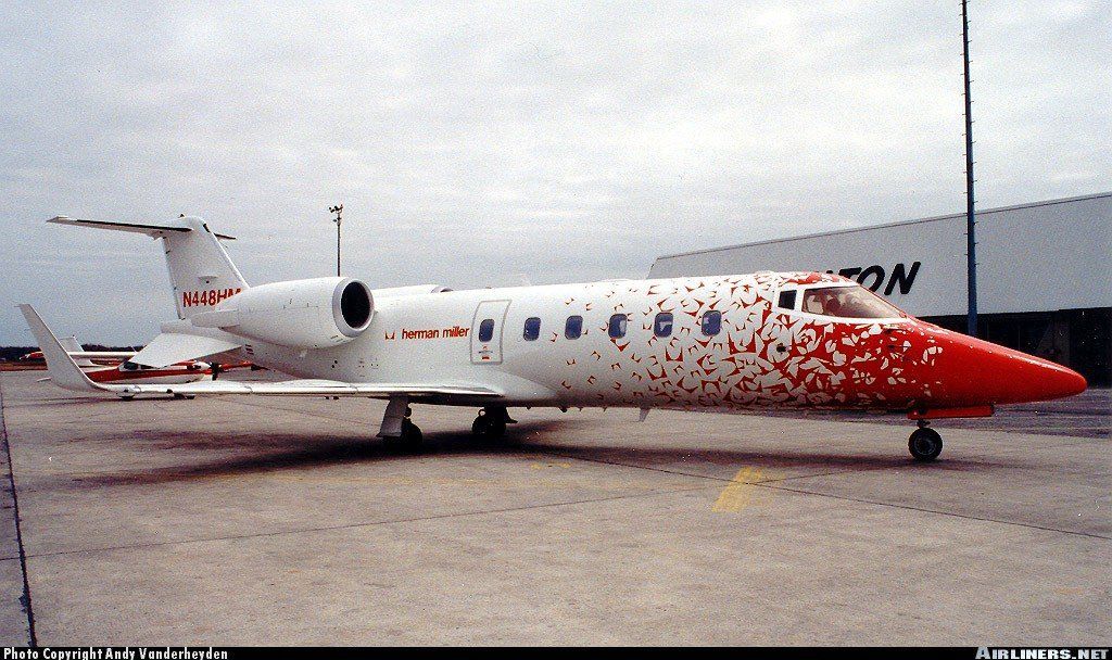 A red and white airplane is parked in front of a building that says no