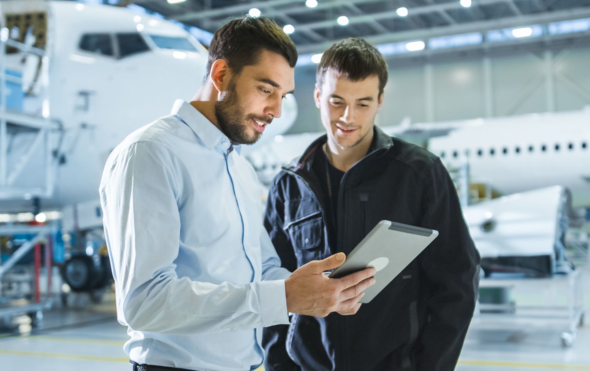 Two men are looking at a tablet in a hangar.