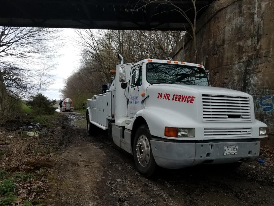 A white tow truck is parked under a bridge on a dirt road.