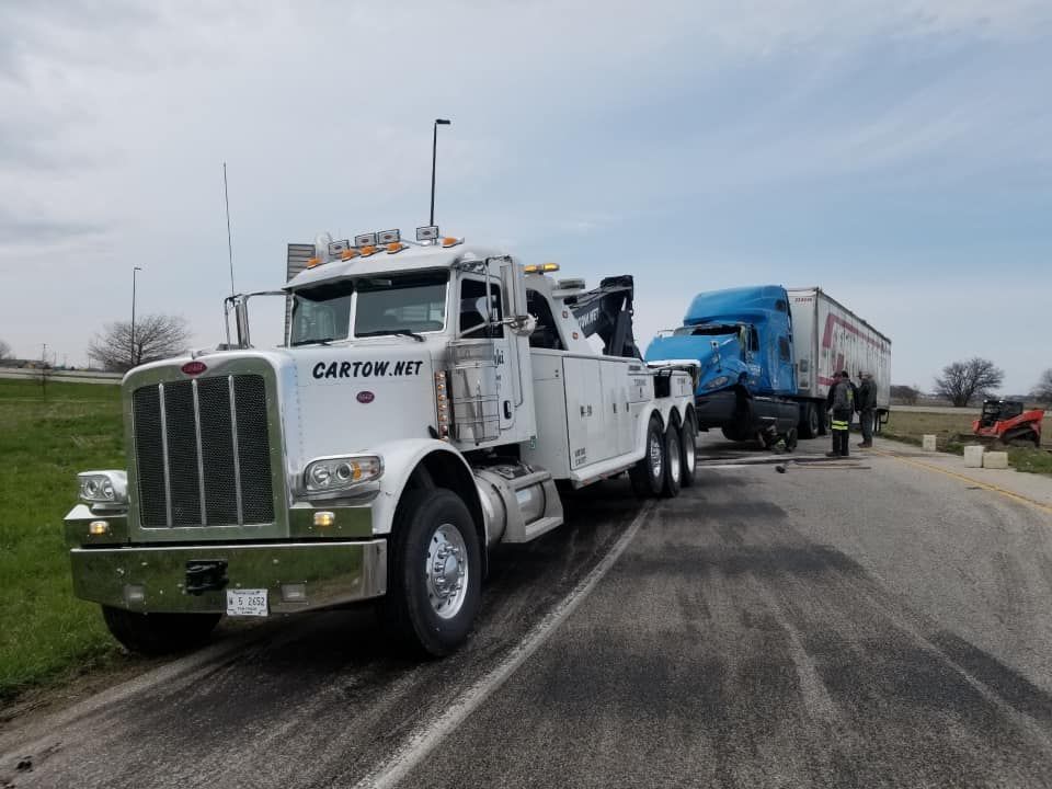 A tow truck is towing a semi truck on the side of the road.