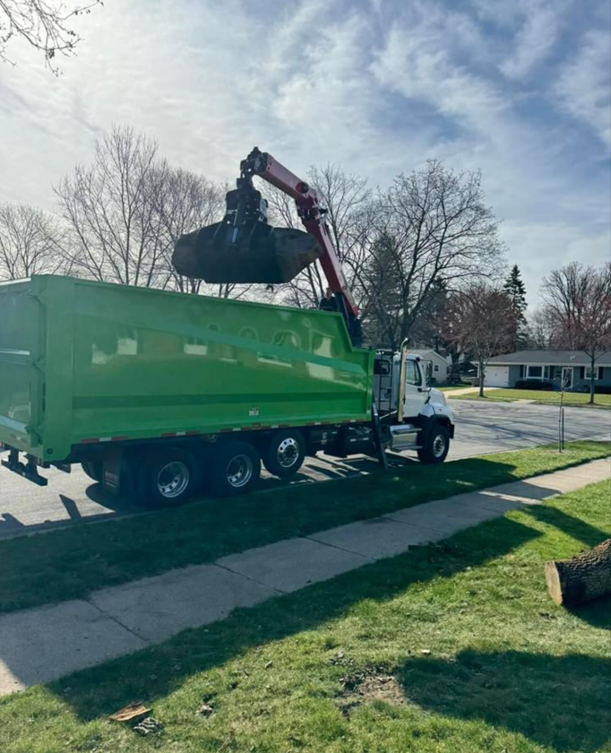 A green dump truck with a crane attached to it is parked on the side of the road.
