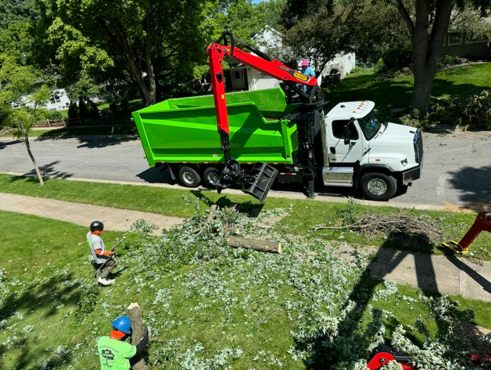 A green dump truck with a crane attached to it is driving down a street.