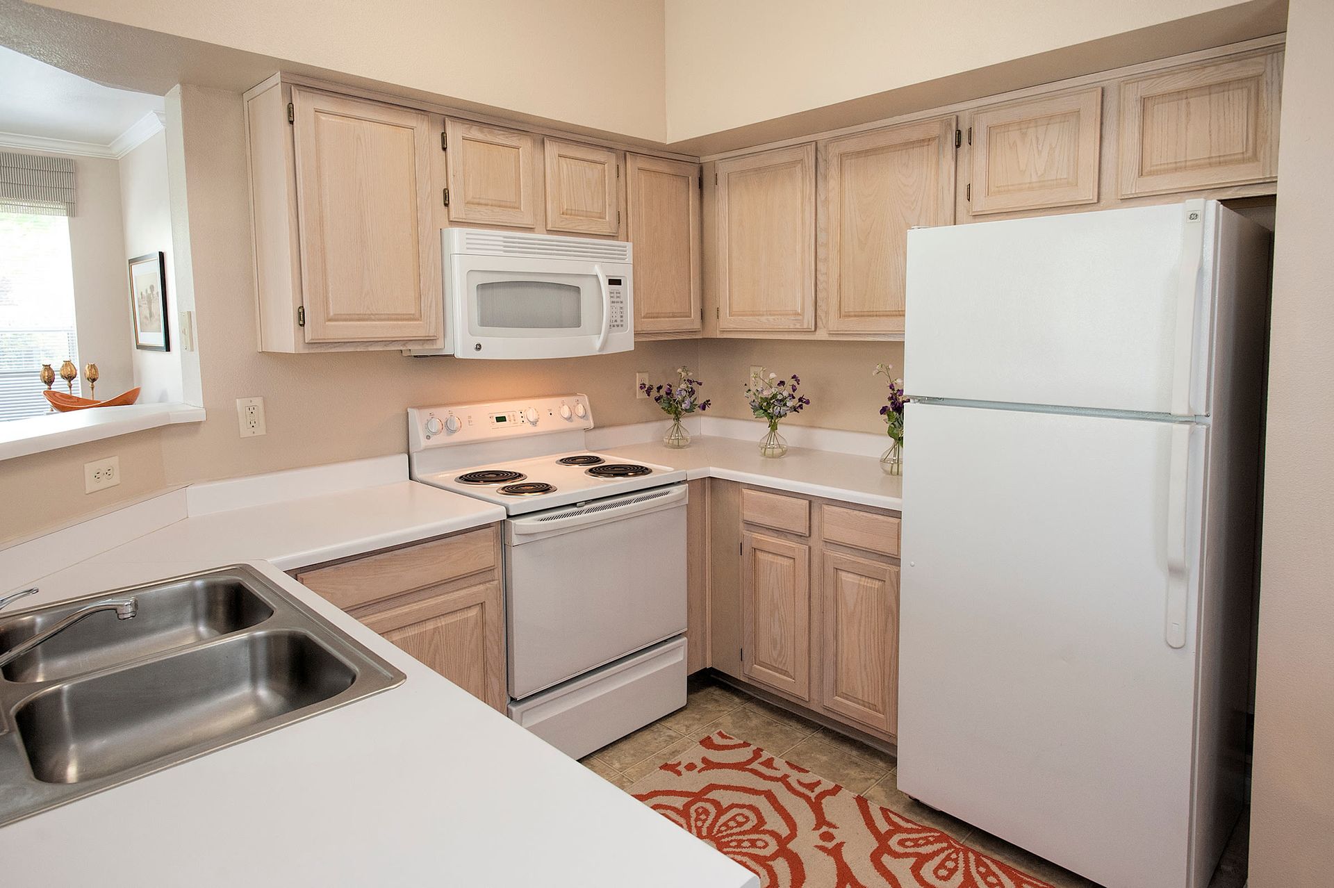 Kitchen with light wooden cabinets, white appliances (stove, microwave, fridge), and double sink.