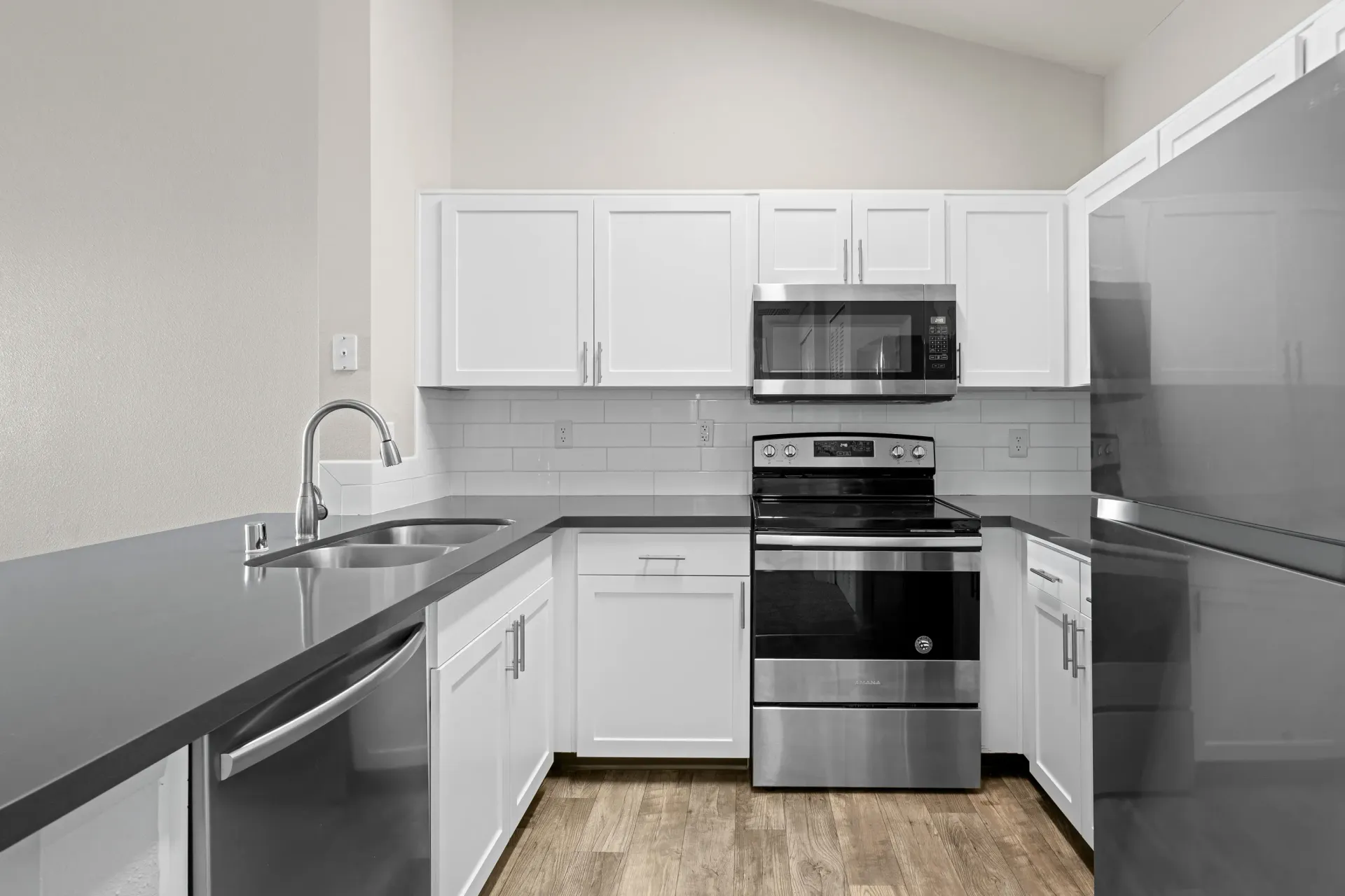Modern kitchen with white cabinets, stainless steel appliances, double-basin sink, gray countertops.