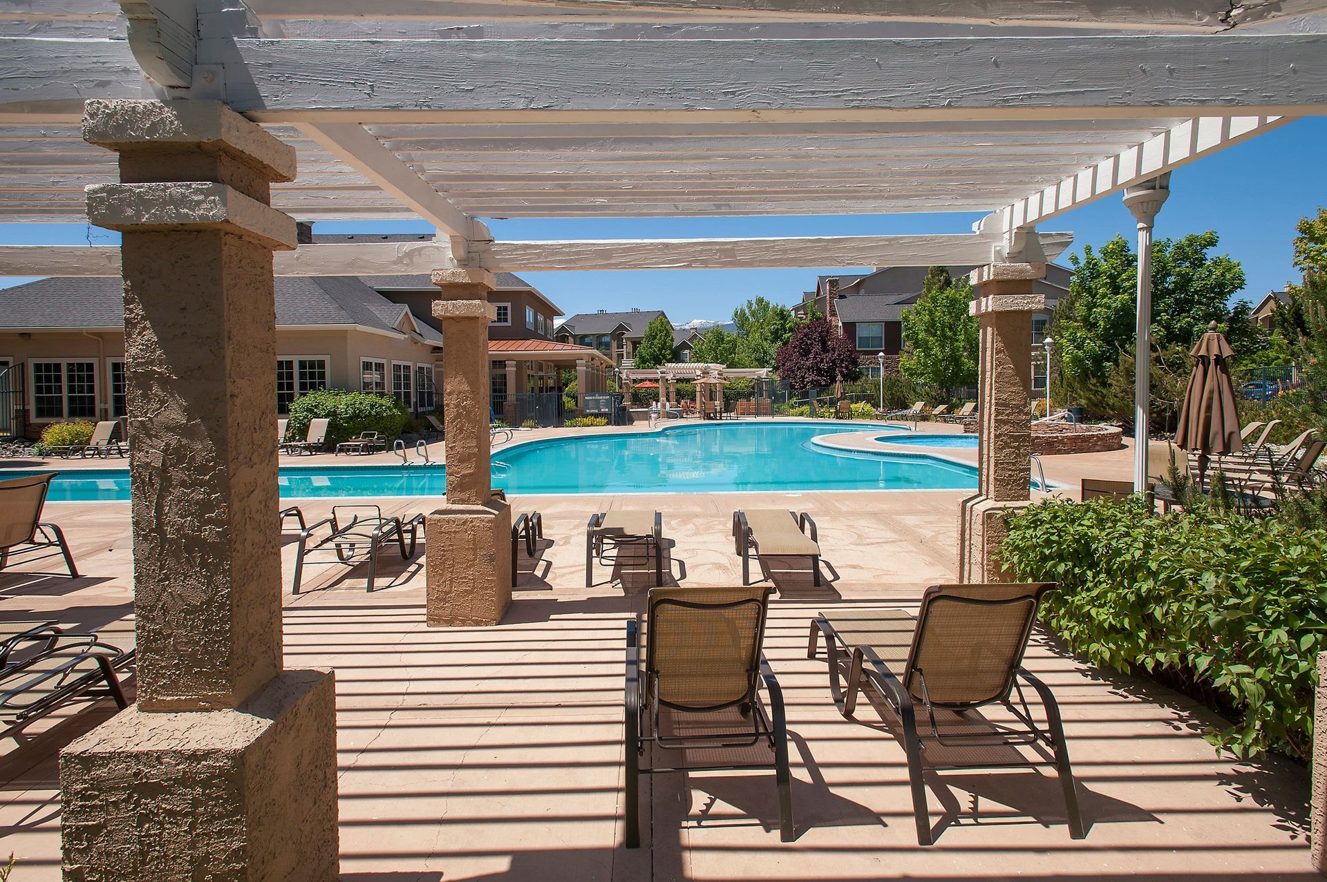 Outdoor pool area with lounge chairs under a white pergola at a residential community