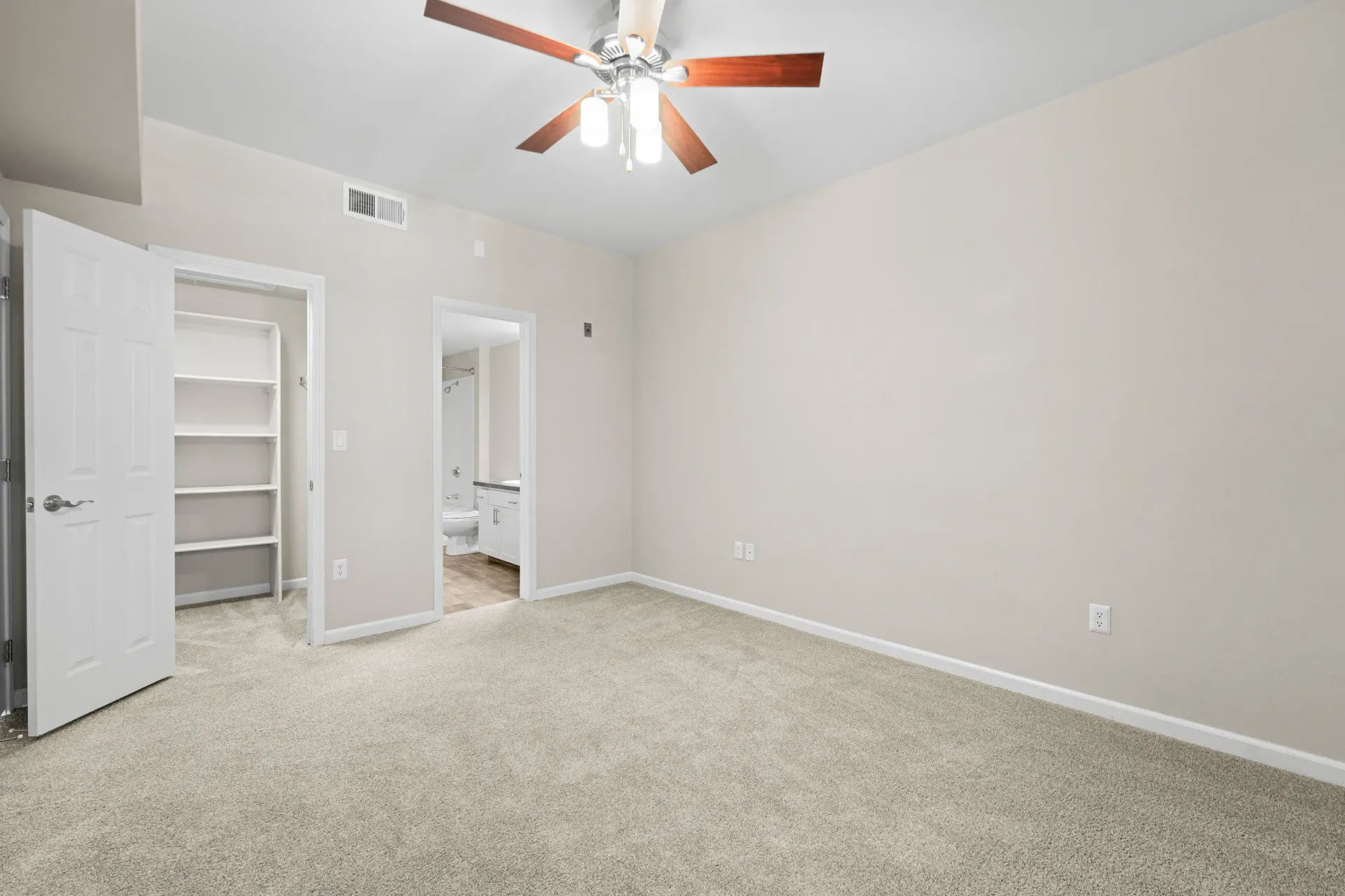 Bedroom with beige walls, carpet, ceiling fan, and walk-in closet.