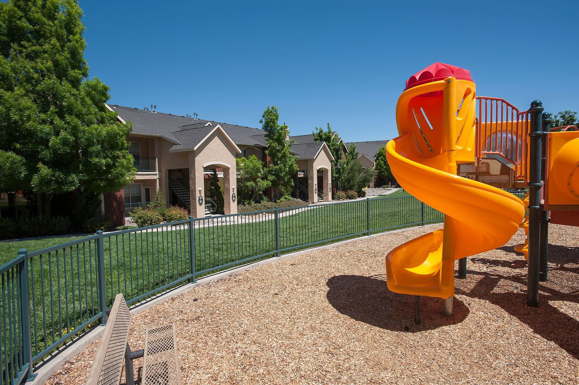 Exterior view of a multifamily community with a bright orange spiral slide and beige buildings.