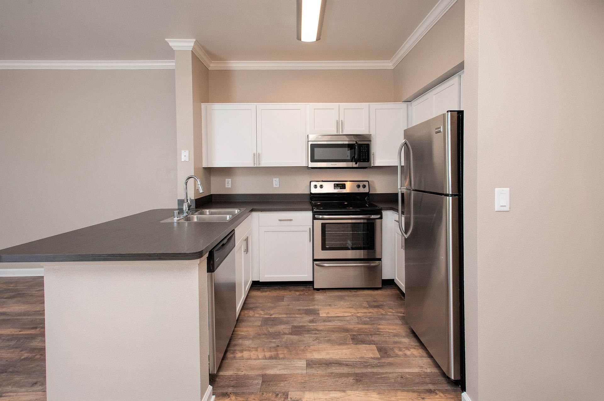 Modern apartment kitchen with stainless steel refrigerator, stove, microwave, white cabinets, and dark countertops.