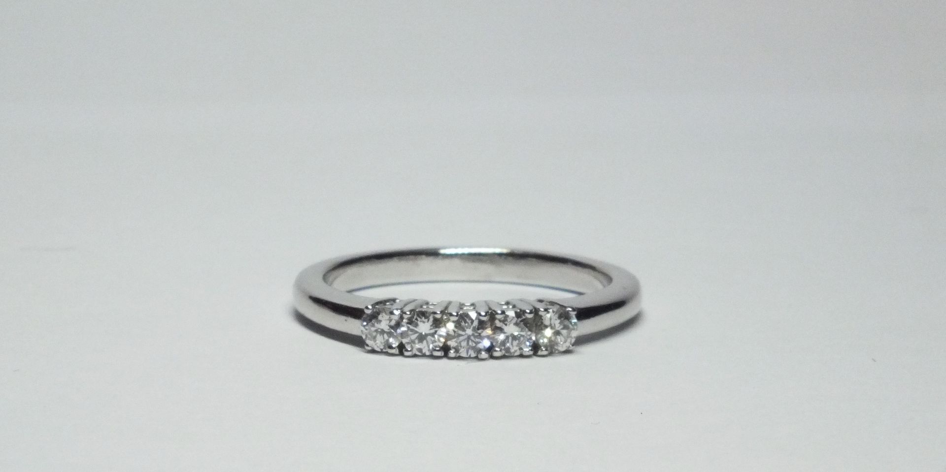 Un anello in oro bianco con diamanti su una superficie bianca.