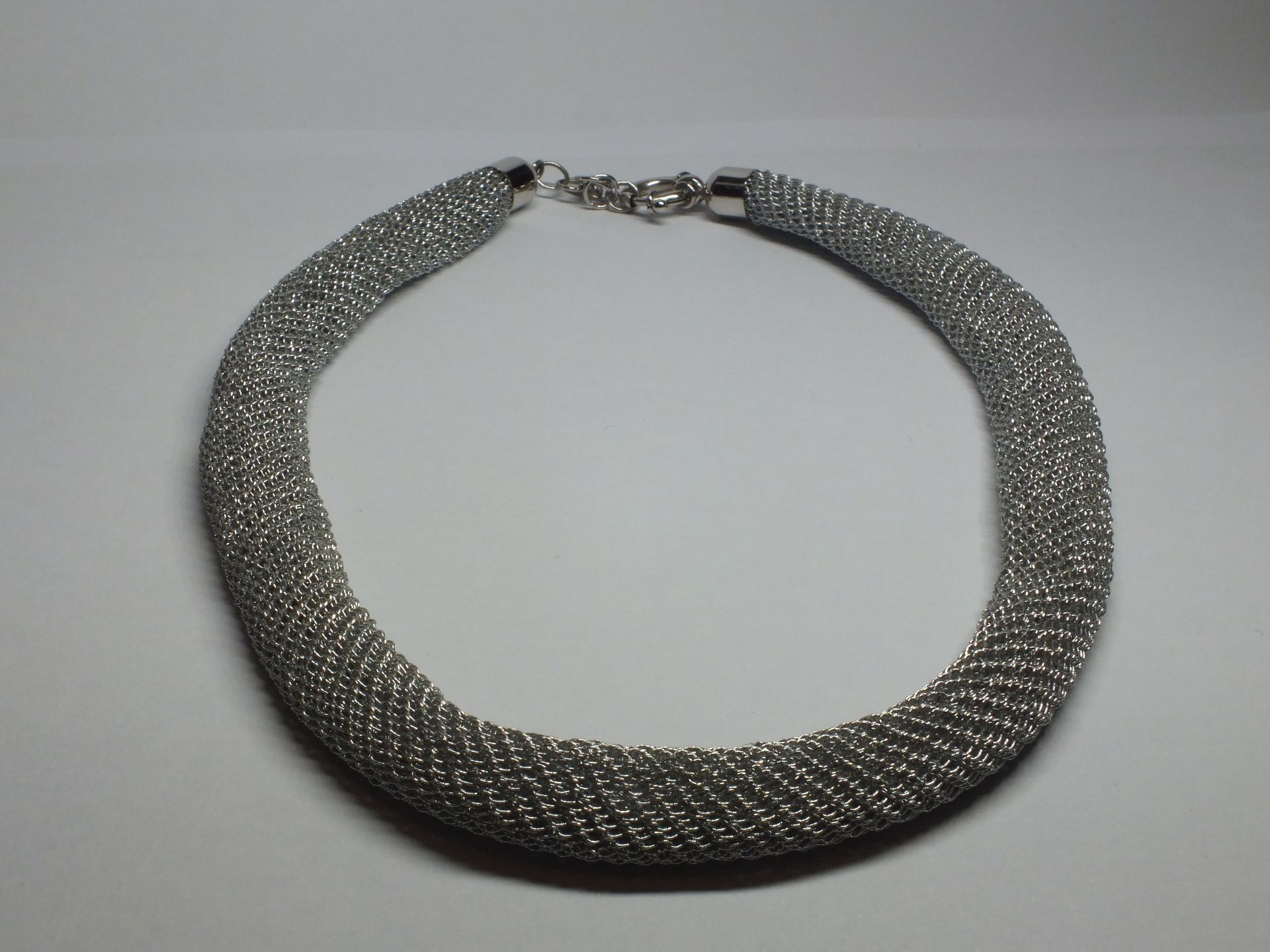 Una collana d'argento è appoggiata su una superficie bianca