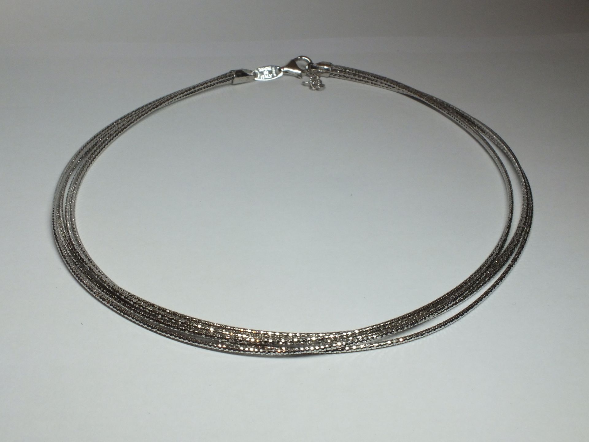 Una collana d'argento è appoggiata su una superficie bianca