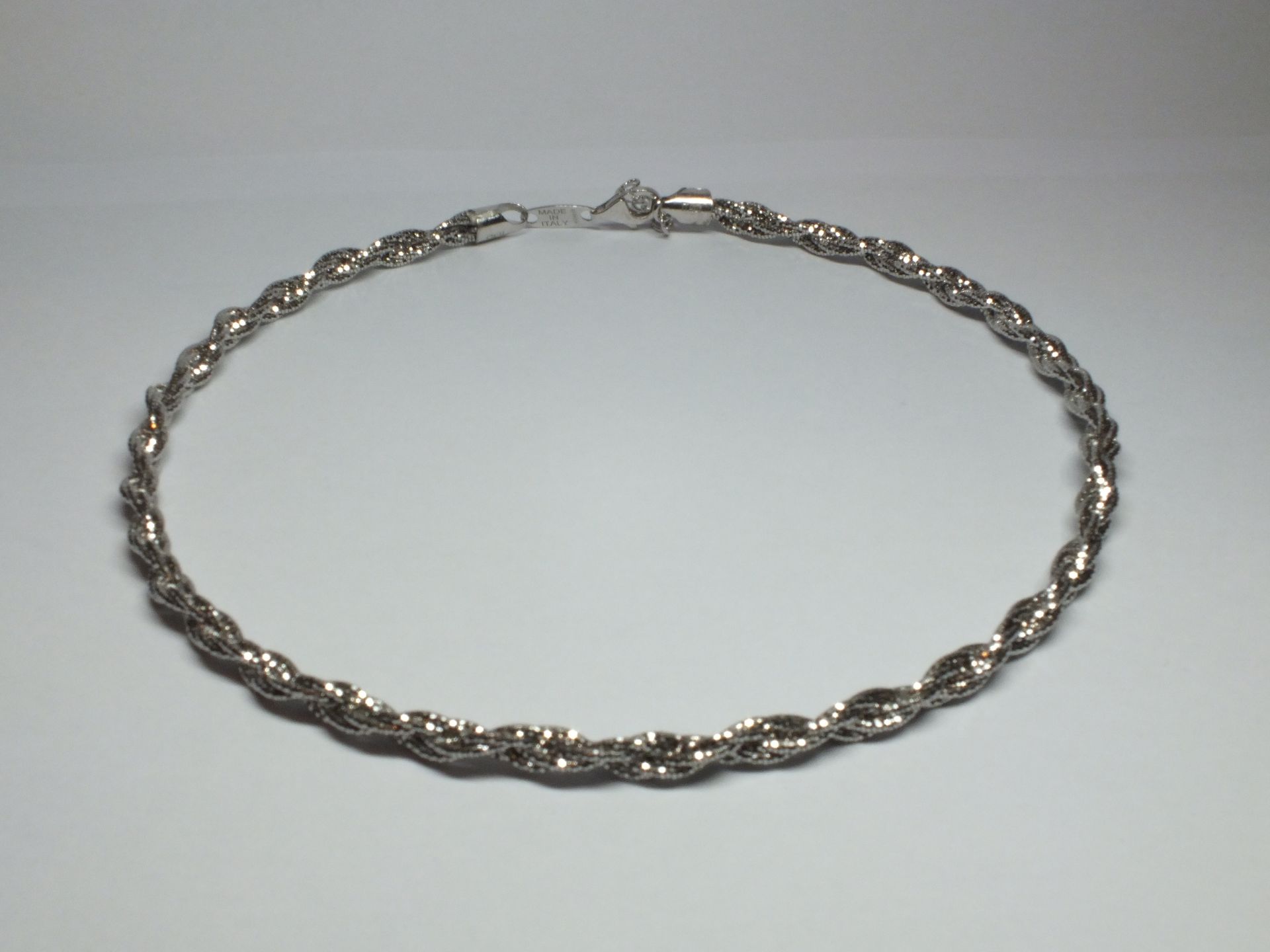 Un braccialetto d'argento è appoggiato su una superficie bianca