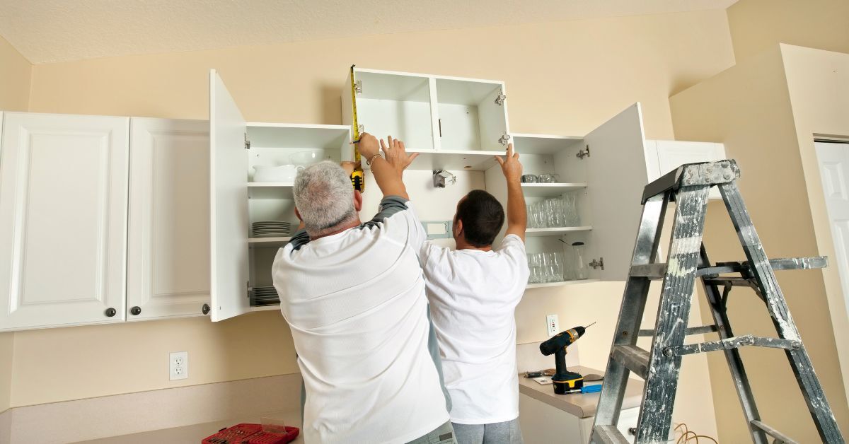 two men are measuring a cabinet in a kitchen .