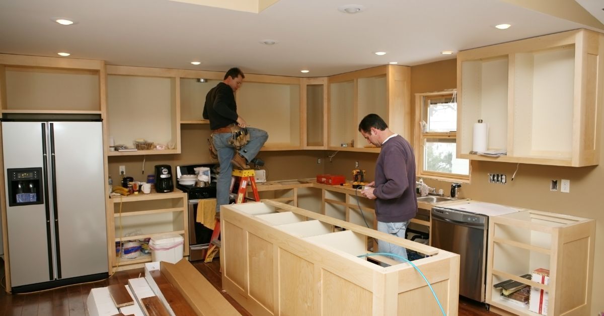 two men are working on a kitchen in a house