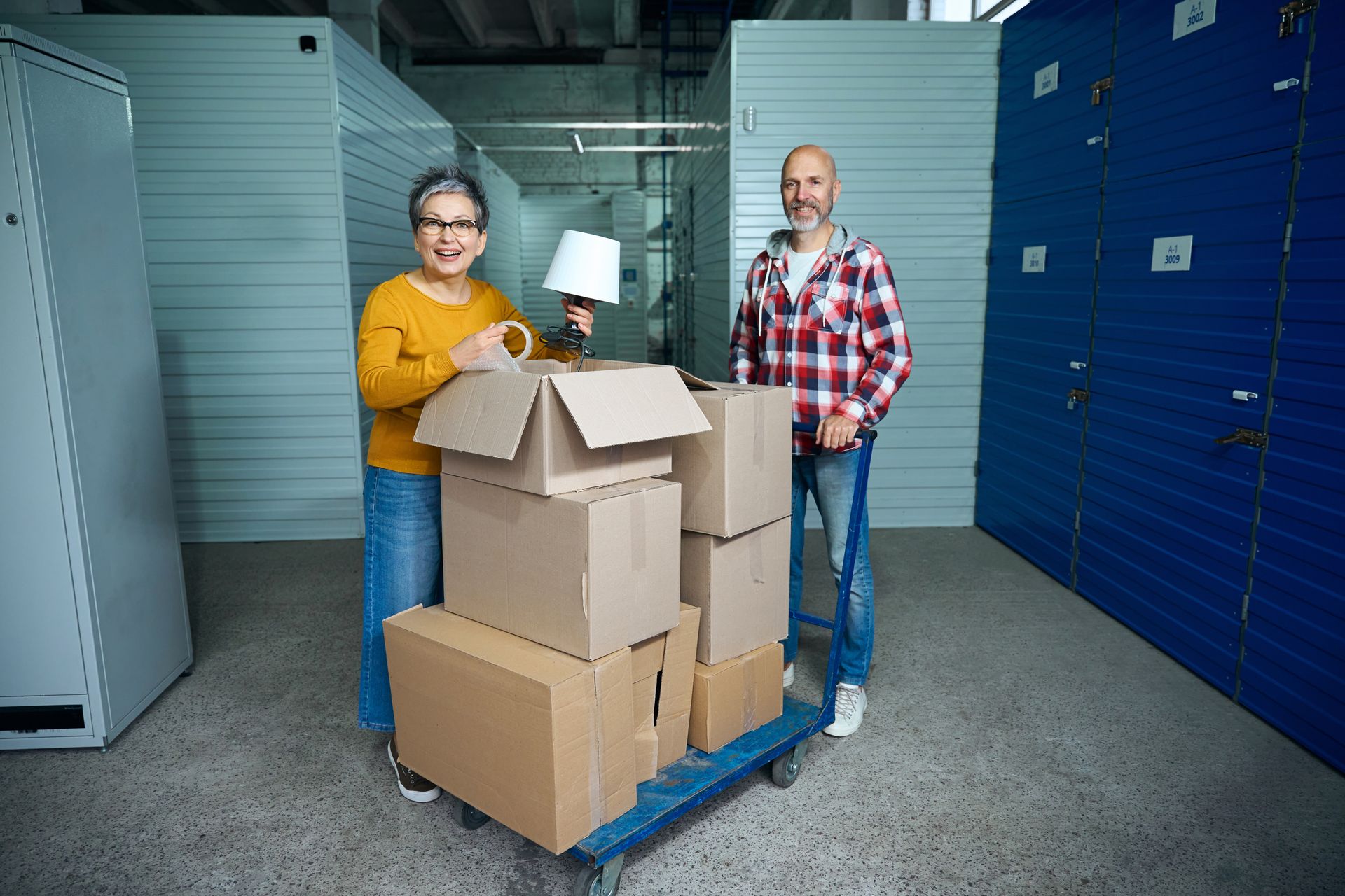 Older couple moving boxes into a self storage unit with a cart.