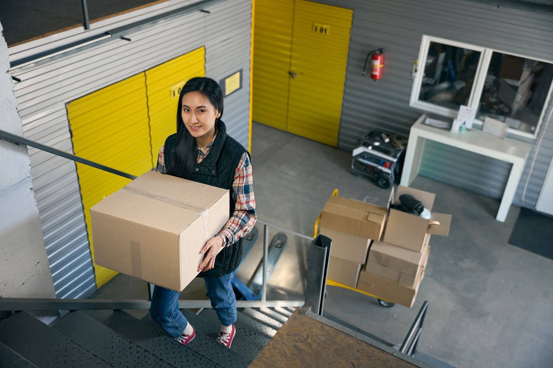 Woman carrying moving boxes inside a self storage facility with yellow roll-up doors
