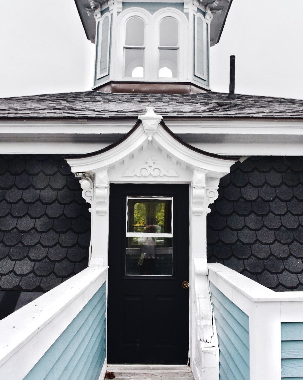 A black door with a white decorative frame leads to a rooftop deck, framed by shingled walls and a small cupola above.
