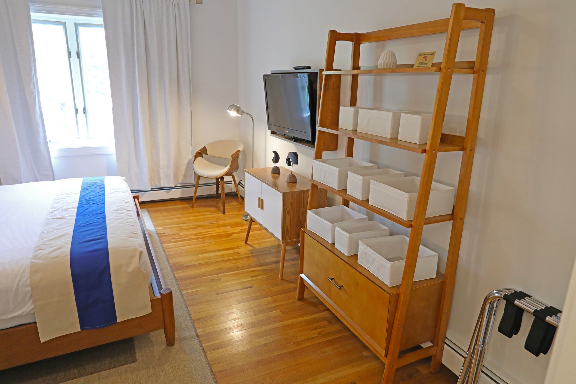 A modern hotel room with a large bed featuring a wooden frame, white linens, and a blue and beige runner.