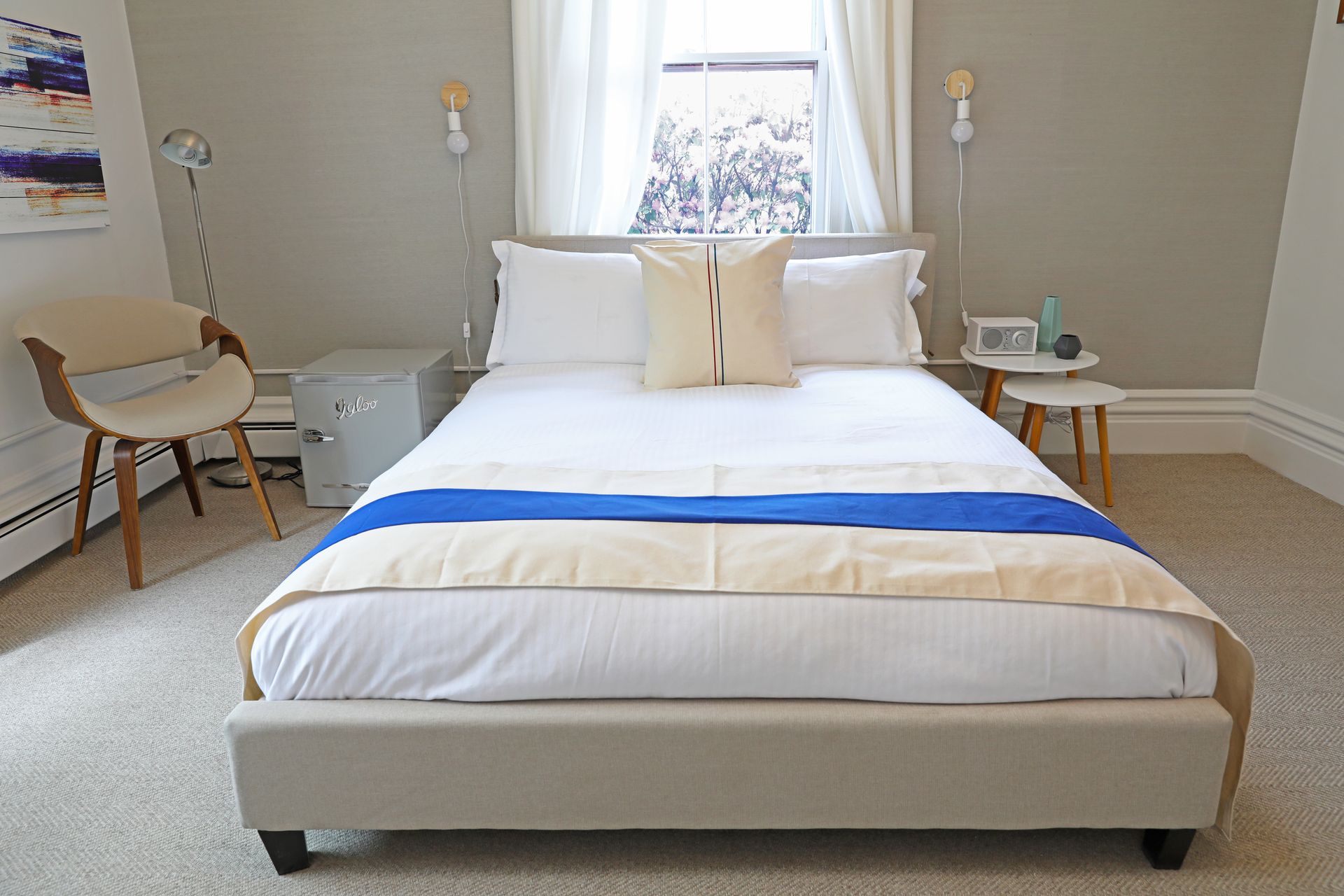 A modern bedroom featuring a bed with white bedding, a bright blue runner, three throw pillows, and a wall map backdrop.