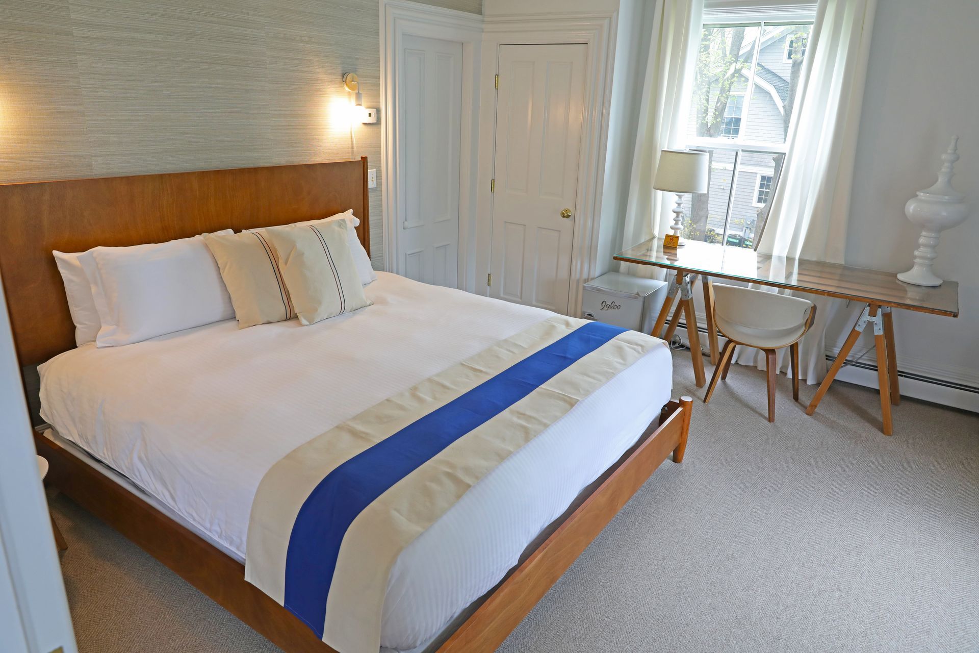 A wooden-framed bed with white bedding, a blue and beige runner, and matching pillows in a room with light carpeting.