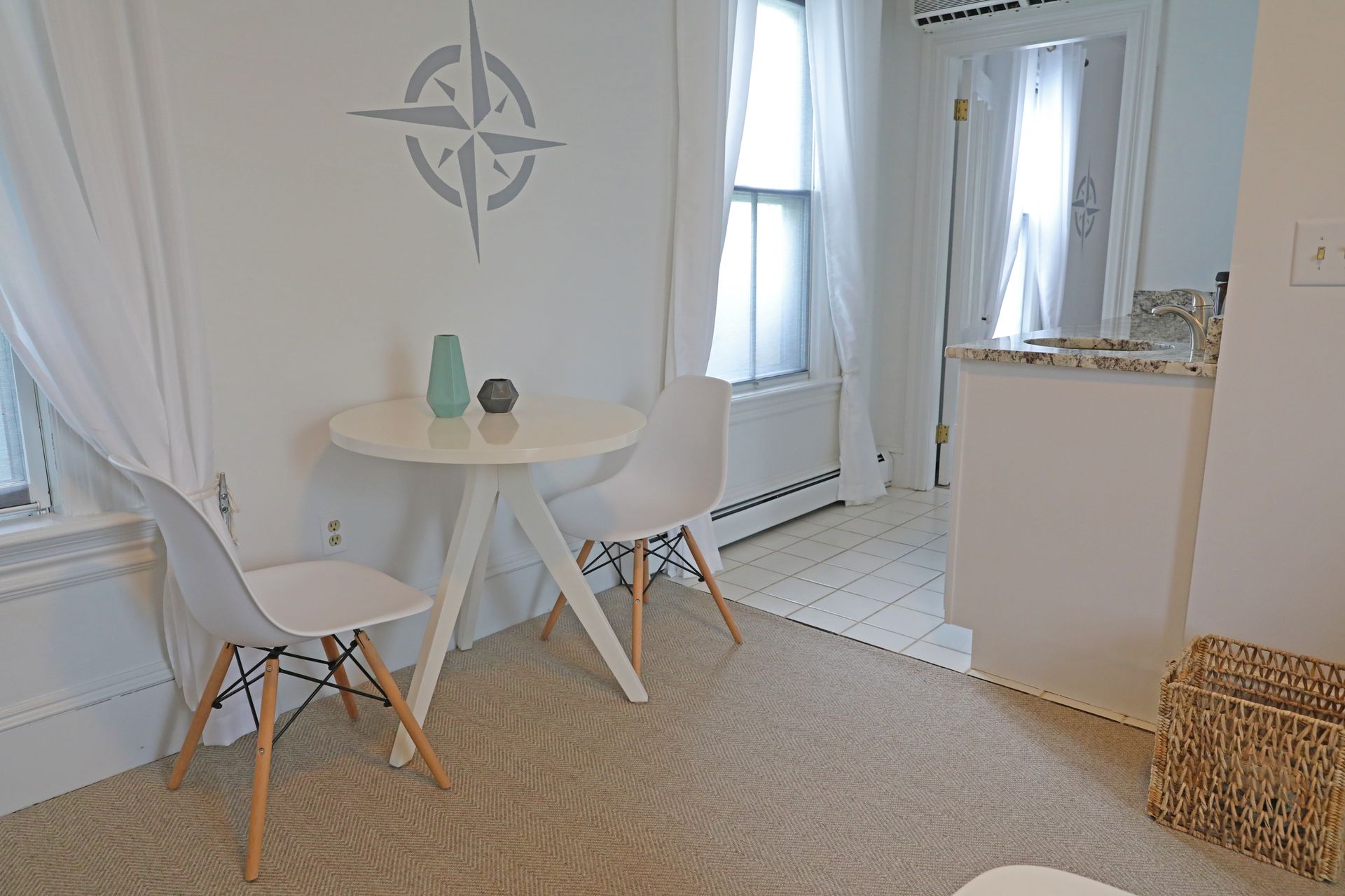 A cozy bedroom with a wooden bed frame, white bedding with a blue stripe, nesting side tables, and a compass wall decal.