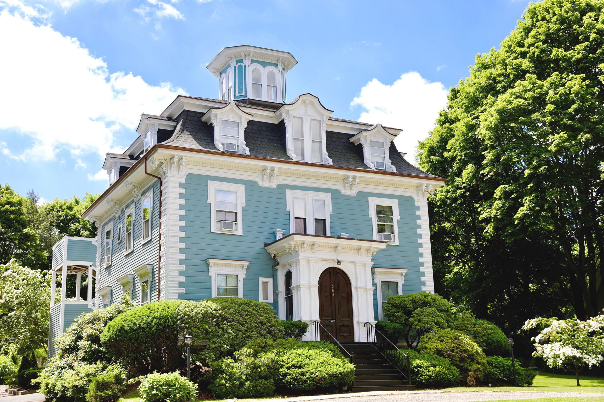 A blue, two-story Victorian-style house with white trim, a mansard roof, dormer windows, and a central cupola.