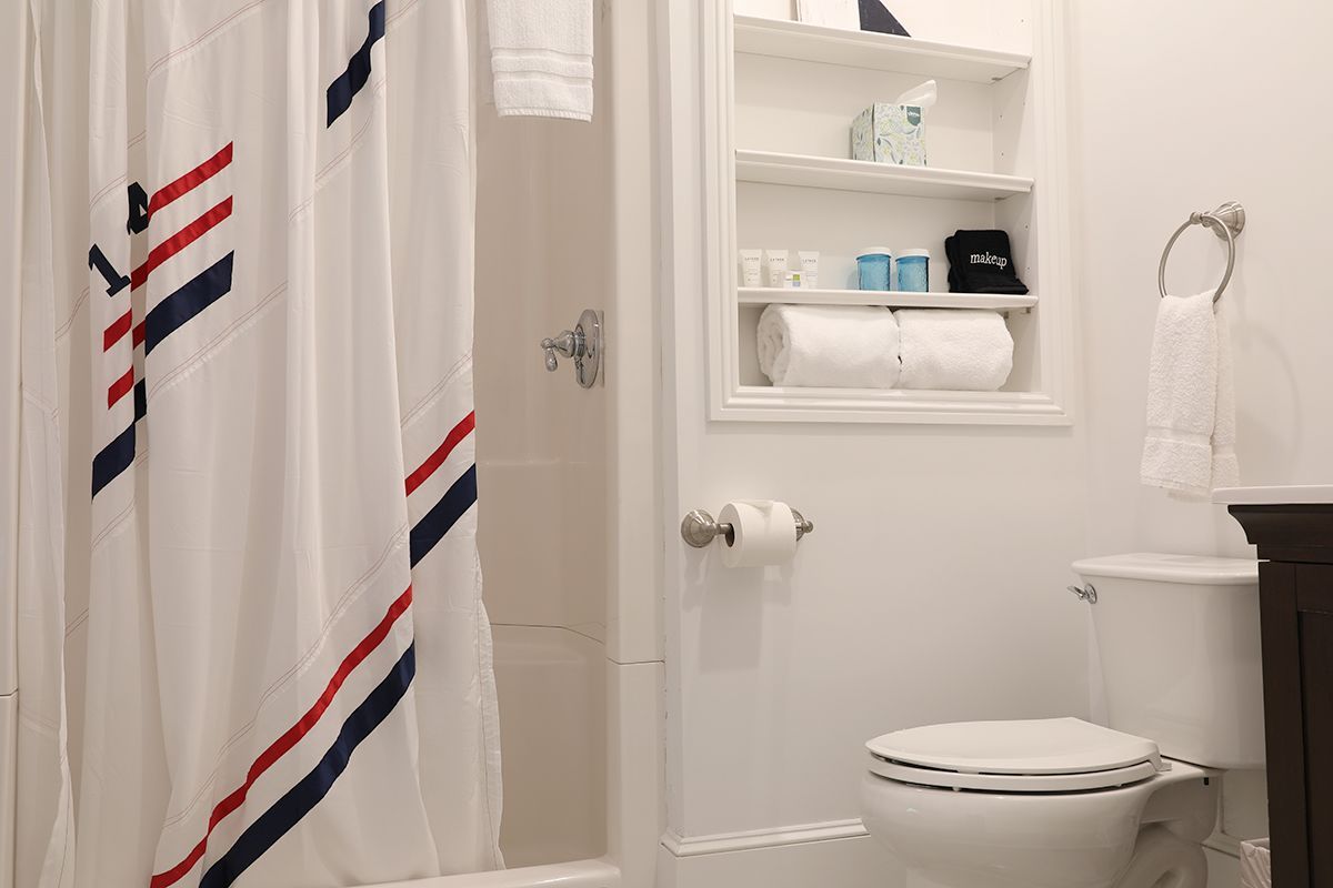 A bathroom with a white shower curtain featuring blue and red stripes, a built-in shelf, a toilet, and a towel on a ring.