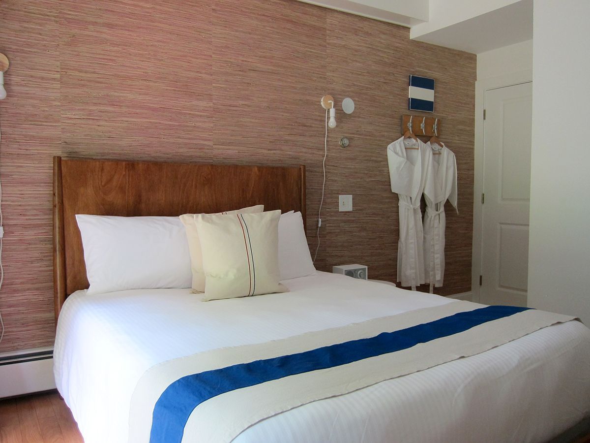 A bedroom featuring a bed with a wooden headboard, white linens, and a blue runner, set against a textured tan wall.