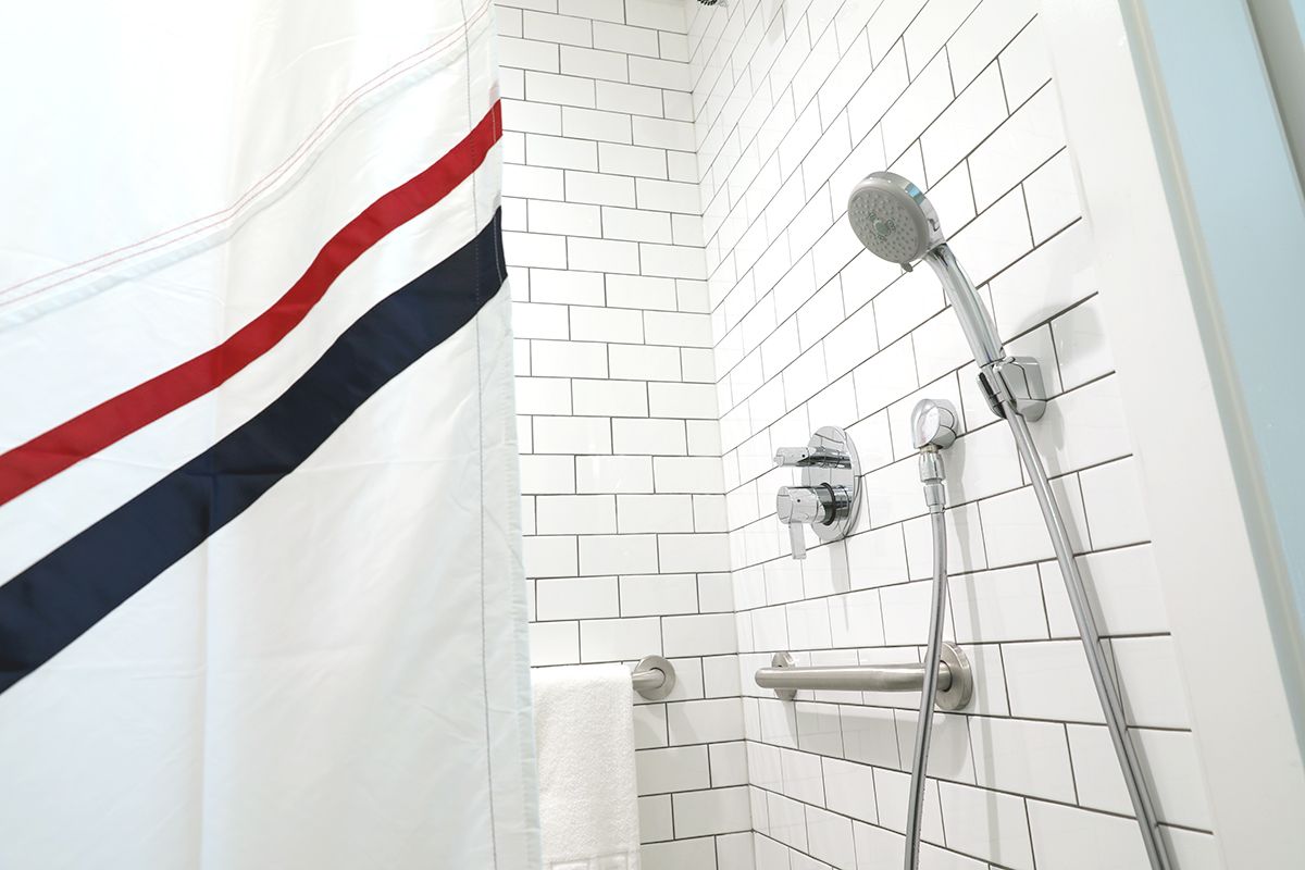 A shower stall with a white and black tiled wall, a chrome handheld shower head, and a white curtain with red and black.