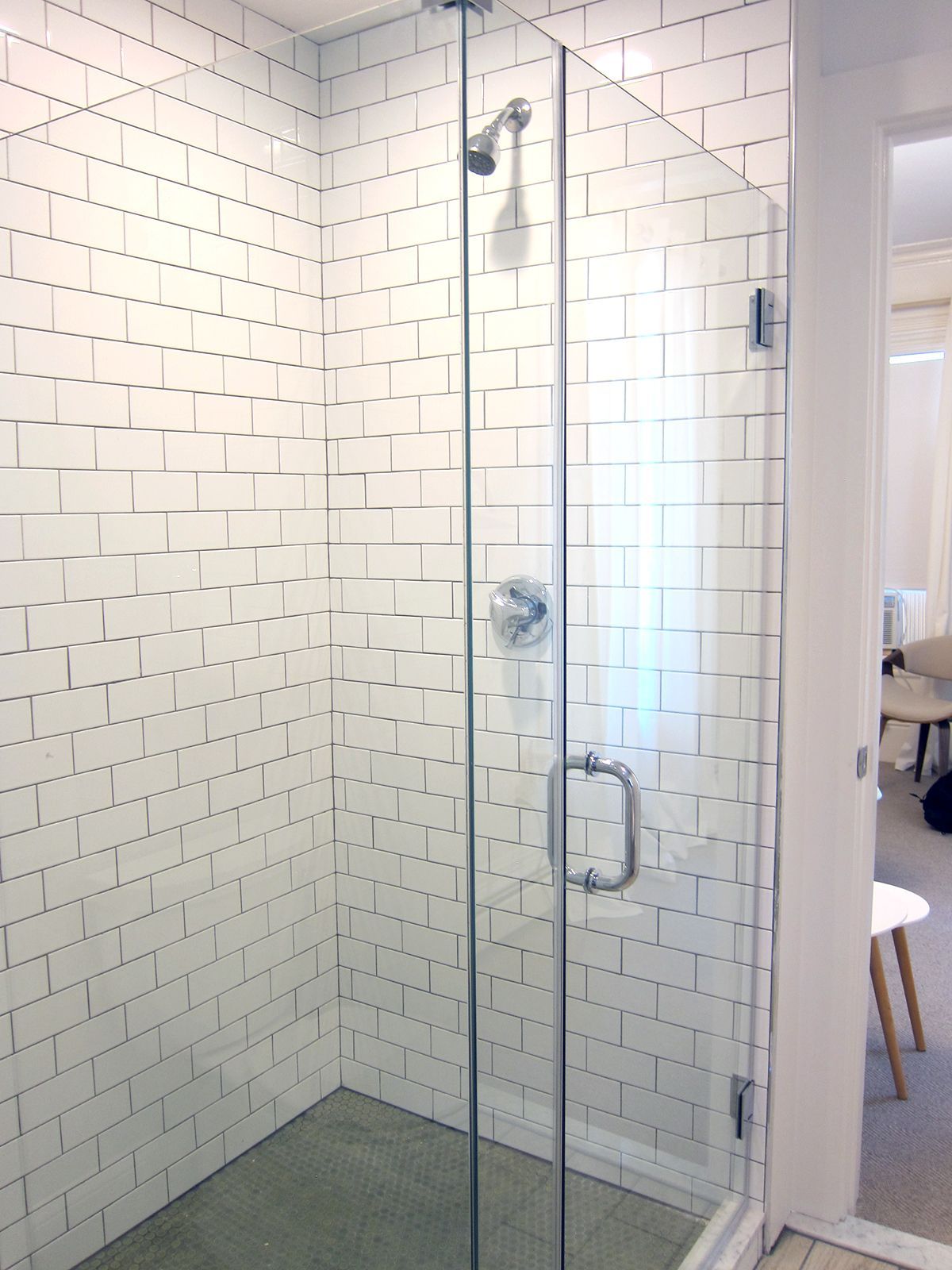 A walk-in shower with white subway-style tiled walls, a glass door, and a modern chrome showerhead and handle.