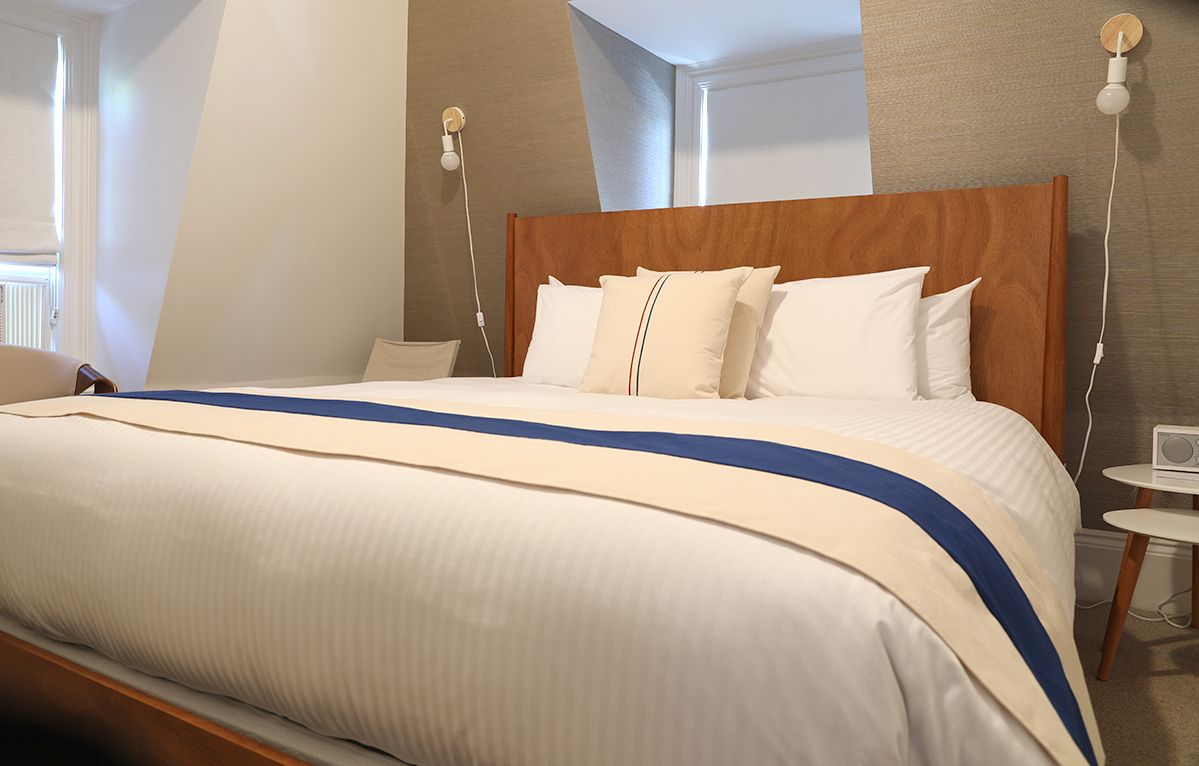 A bedroom with a king-sized bed featuring a wooden headboard, white bedding, and a blue and cream runner.