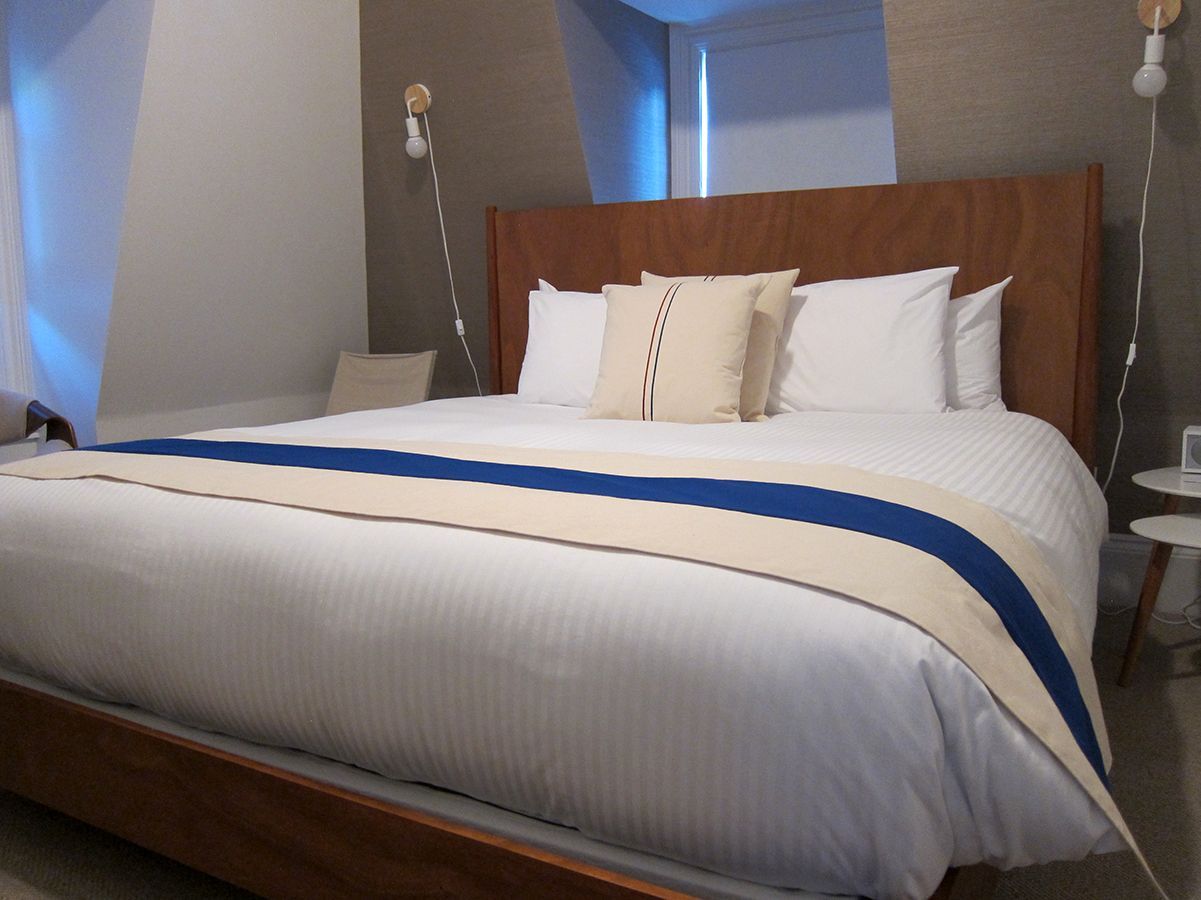 A modern bed with white bedding and a blue-and-tan runner, placed against a wood headboard in a contemporary room.