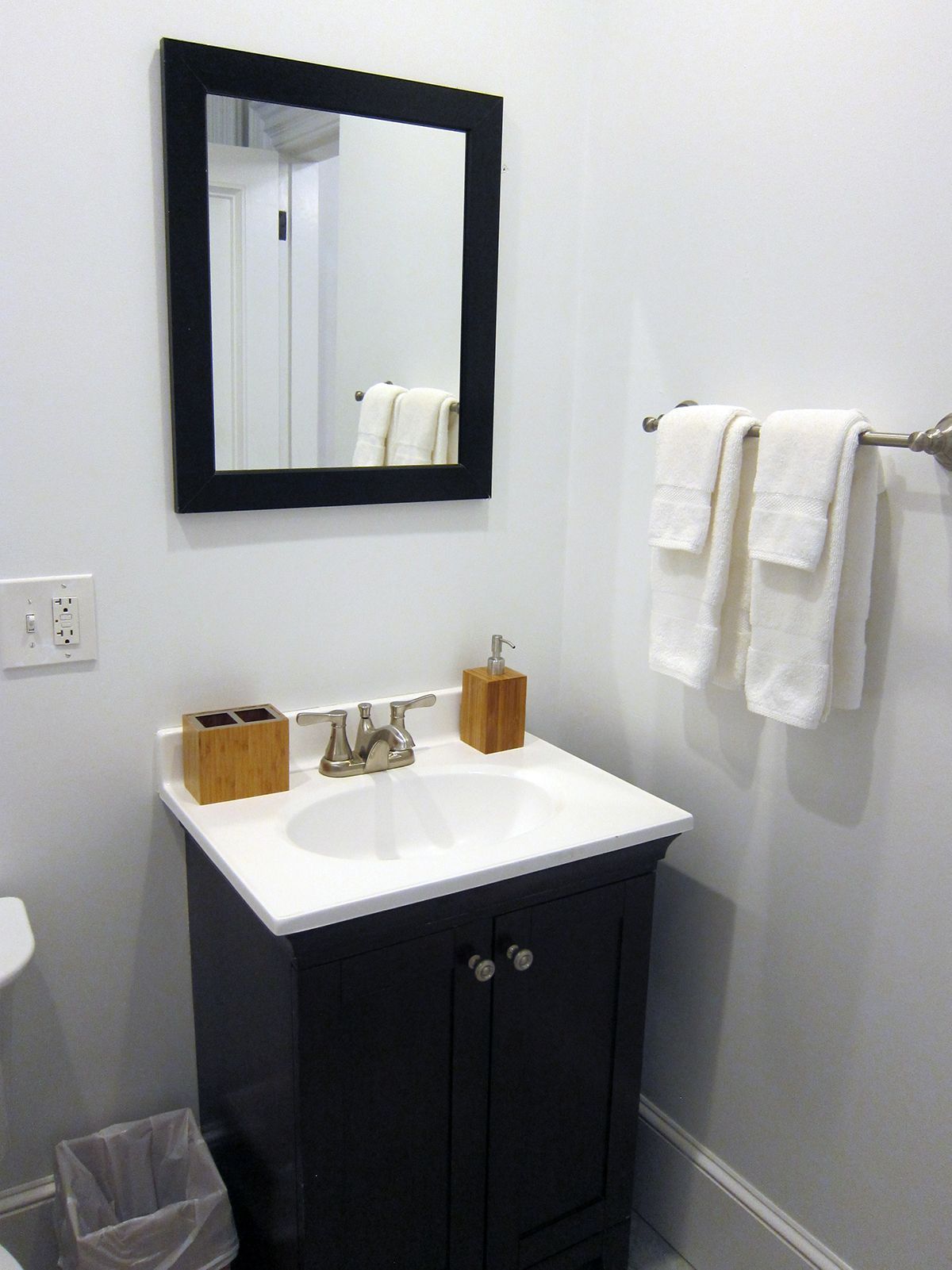 A bathroom vanity with a dark wood cabinet, white sink, black-framed mirror, and two white towels on a wall rack.