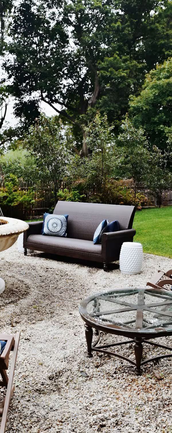 Outdoor patio area with a dark wicker sofa, patterned throw pillows, a round glass-top table, and a white side stool.