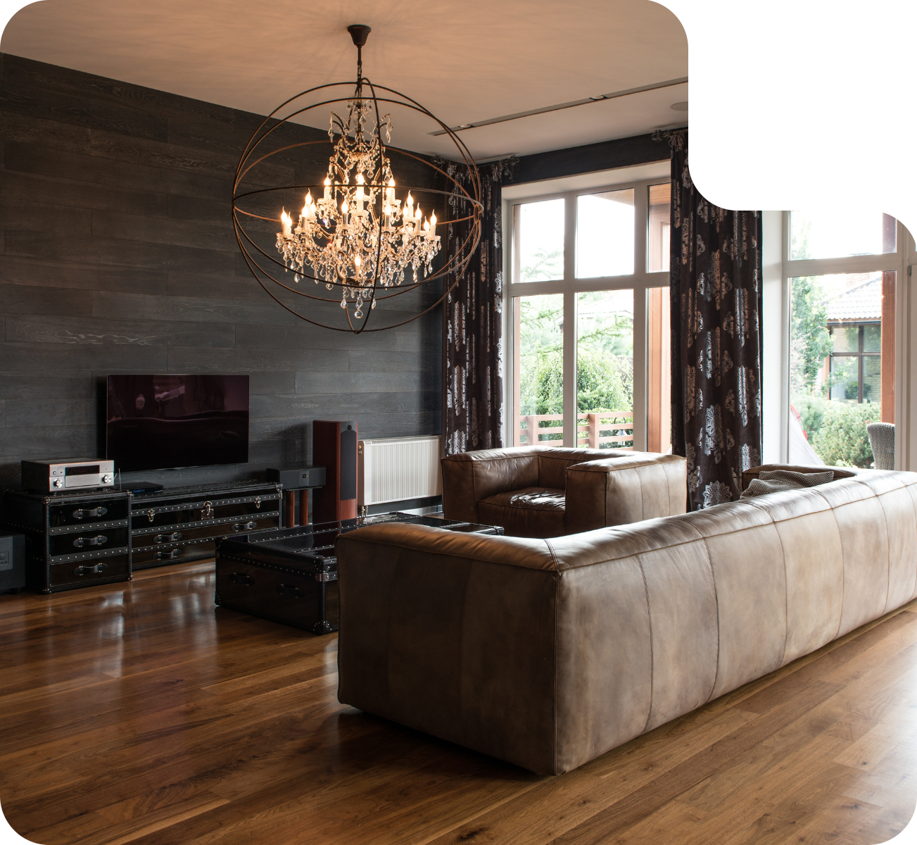 Living room with leather sofa, chandelier, and large windows. Wooden floors and dark accent wall.
