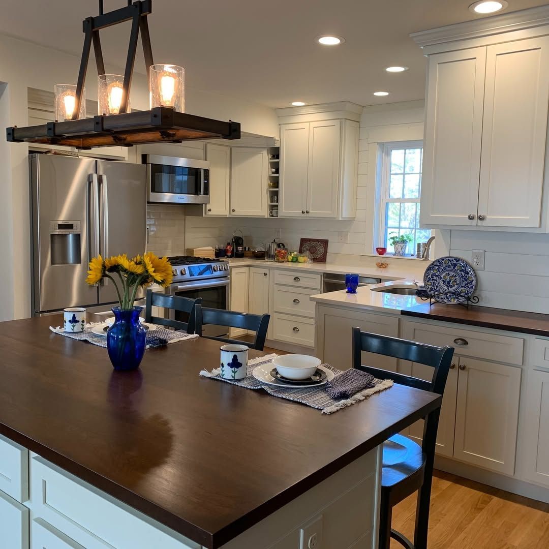 Bright kitchen with wooden island, white cabinets, stainless steel appliances, and a hanging light fixture.